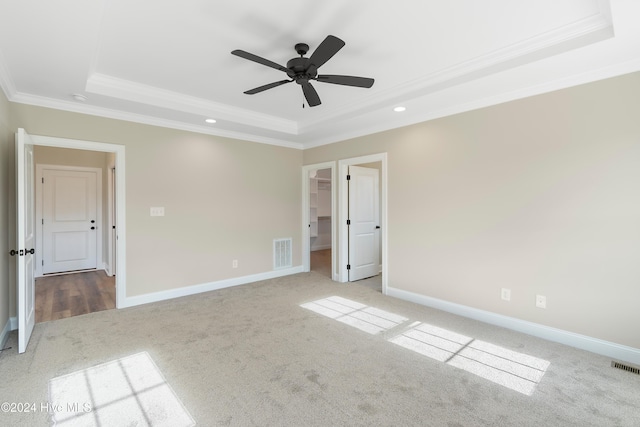 unfurnished bedroom with ceiling fan, light colored carpet, ornamental molding, and a tray ceiling