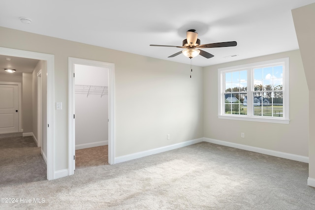 unfurnished bedroom with a walk in closet, light colored carpet, a closet, and ceiling fan