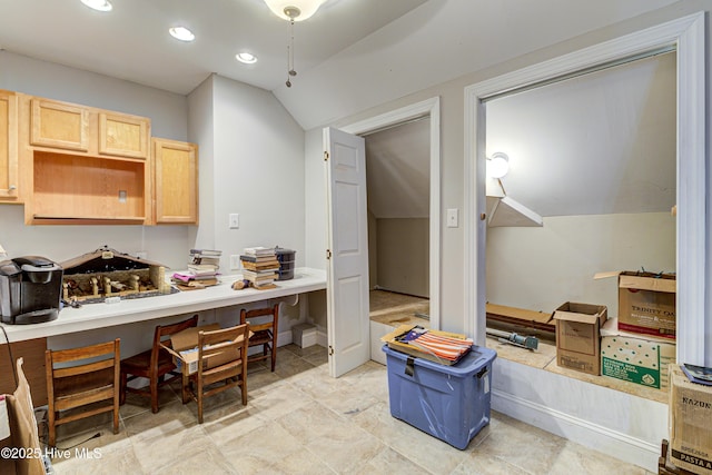 interior space with vaulted ceiling, light brown cabinets, and built in desk