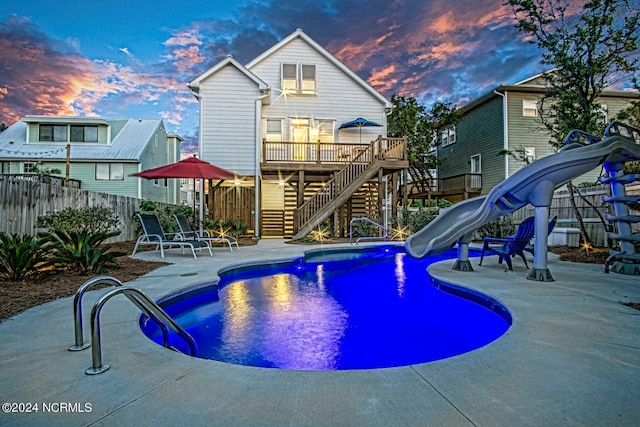 pool at dusk featuring a patio and a water slide