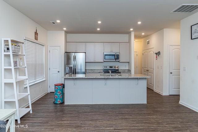 kitchen featuring dark hardwood / wood-style floors, stainless steel appliances, light stone countertops, a kitchen island with sink, and white cabinets