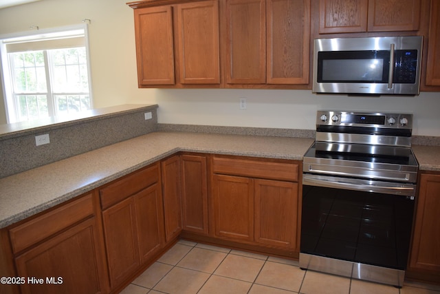 7304 E Oak Island Dr, Oak Island, NC 28465 - kitchen featuring stainless steel appliances, brown cabinetry, light tile patterned floors, and light countertops
