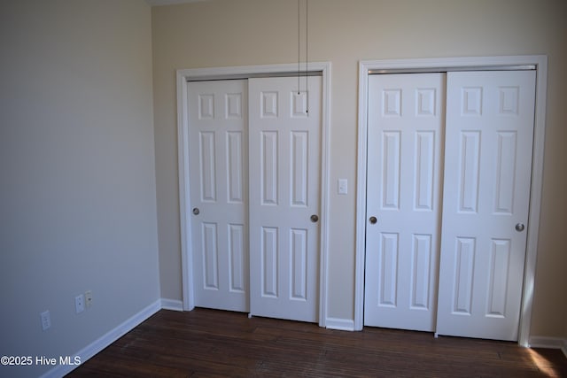 7304 E Oak Island Dr, Oak Island, NC 28465 - unfurnished bedroom featuring two closets, baseboards, and dark wood-style flooring