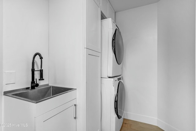 laundry area featuring cabinets, stacked washer and clothes dryer, sink, and light hardwood / wood-style flooring