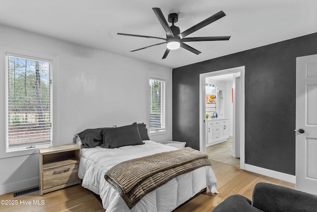 bedroom with multiple windows, ceiling fan, connected bathroom, and light wood-type flooring