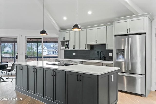 kitchen with gray cabinets, pendant lighting, stainless steel fridge, black electric stovetop, and light stone countertops