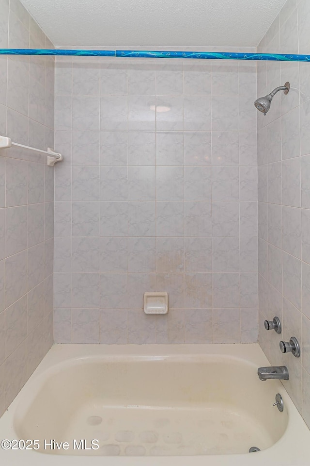 bathroom with tiled shower / bath combo and a textured ceiling