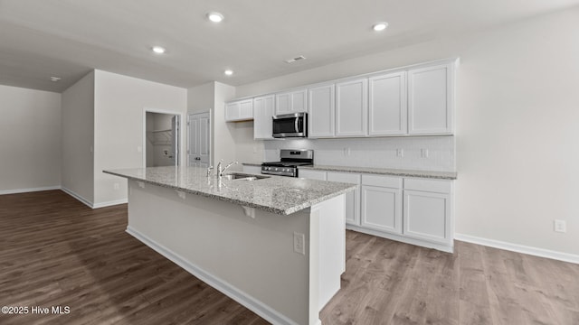 kitchen with light stone counters, stainless steel appliances, an island with sink, and white cabinets