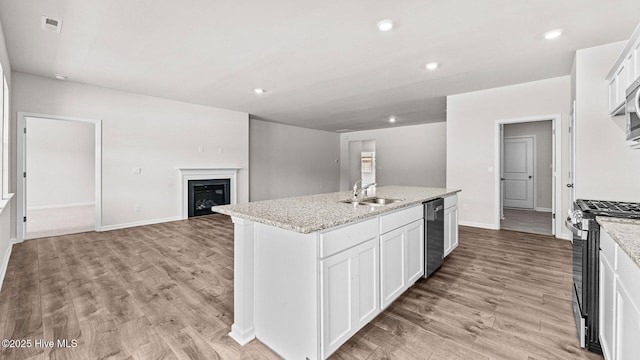 kitchen with appliances with stainless steel finishes, sink, white cabinets, a kitchen island with sink, and light stone countertops