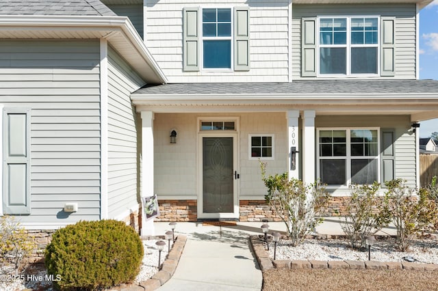 view of exterior entry featuring a porch and a shingled roof