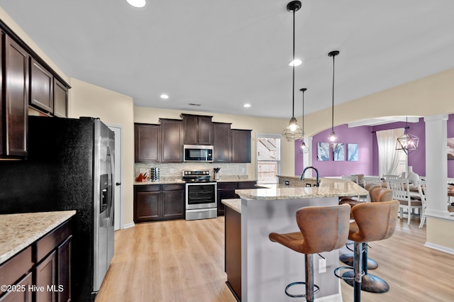 300 William Sharp Way, Jacksonville, NC 28546 - kitchen featuring appliances with stainless steel finishes, a breakfast bar area, dark brown cabinets, light wood-style floors, and decorative backsplash