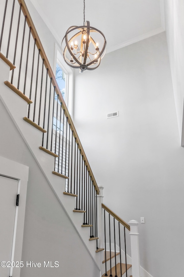 stairs with an inviting chandelier, visible vents, and ornamental molding