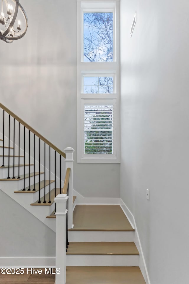 staircase with visible vents, wood finished floors, a high ceiling, an inviting chandelier, and baseboards