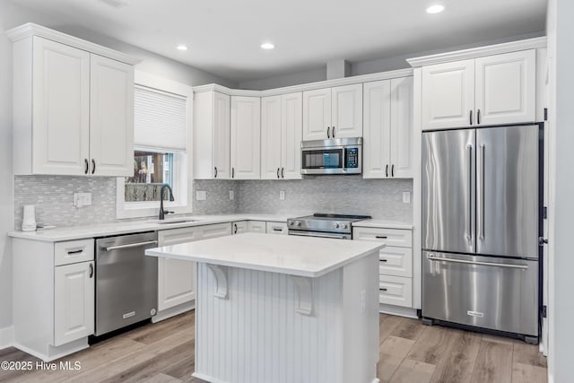 kitchen featuring a sink, a kitchen island, light wood-style floors, appliances with stainless steel finishes, and white cabinets