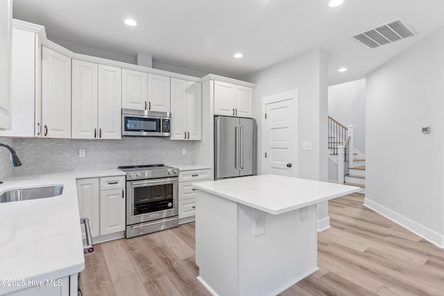 kitchen featuring visible vents, a kitchen island, white cabinets, stainless steel appliances, and a sink