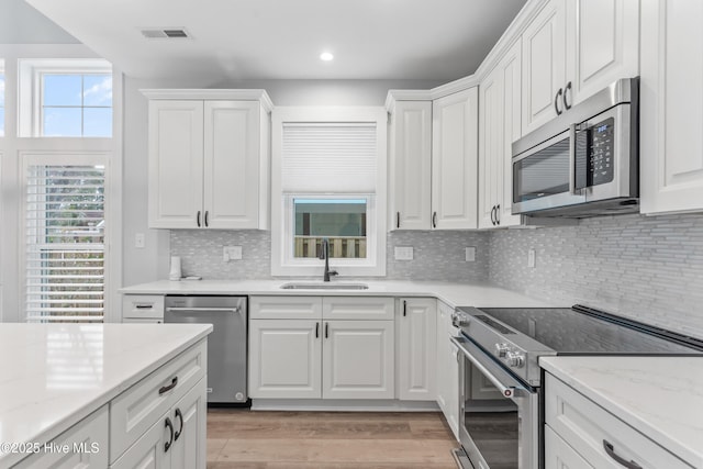 kitchen with visible vents, light wood-style flooring, white cabinets, stainless steel appliances, and a sink