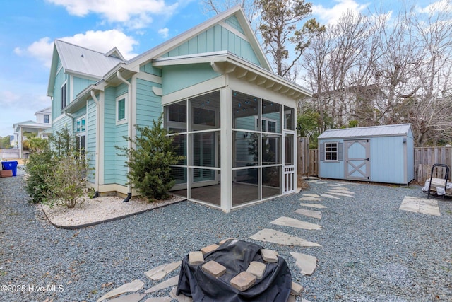 rear view of house featuring an outbuilding, fence, a shed, board and batten siding, and a sunroom