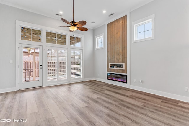 interior space with a glass covered fireplace, crown molding, light wood-style floors, and visible vents