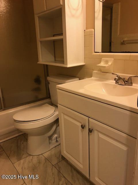 full bathroom with tile walls, backsplash, bath / shower combo with glass door, vanity, and toilet