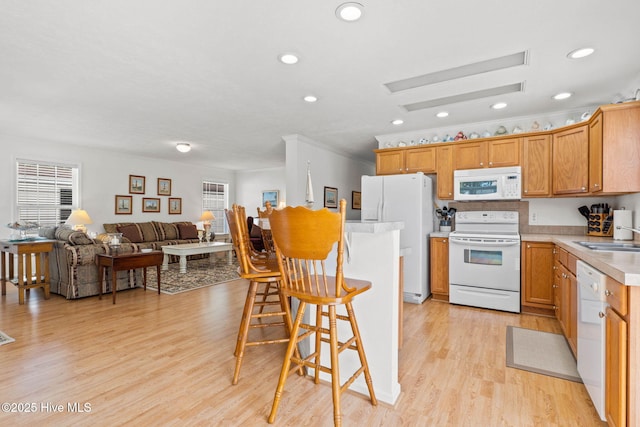 kitchen featuring a breakfast bar, sink, crown molding, white appliances, and light hardwood / wood-style floors