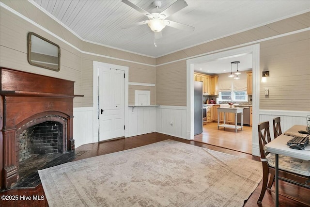 living area with a fireplace with flush hearth, light wood-type flooring, a wainscoted wall, and crown molding