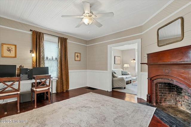 office space featuring a fireplace with flush hearth, a ceiling fan, ornamental molding, wainscoting, and wood finished floors