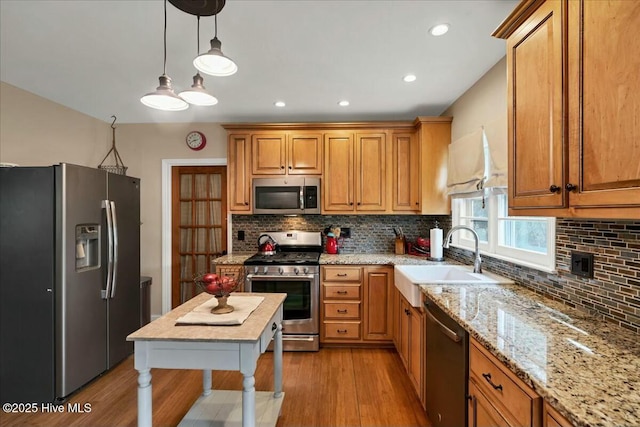 kitchen with backsplash, light wood-style flooring, appliances with stainless steel finishes, a sink, and light stone countertops