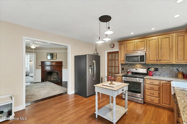 kitchen with stainless steel appliances, light wood-type flooring, a fireplace, and decorative backsplash