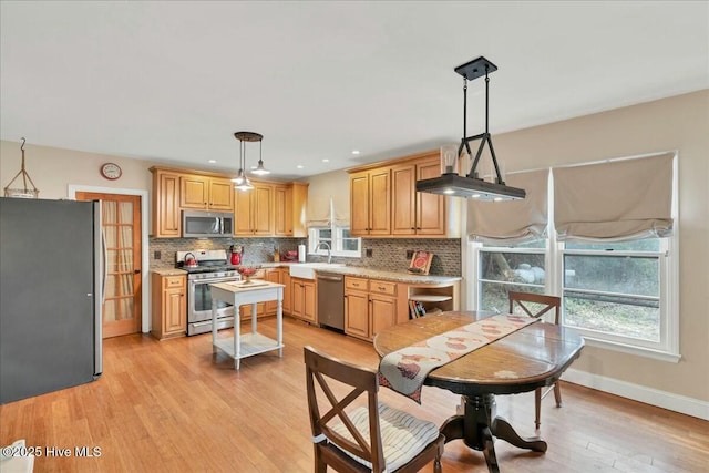 kitchen featuring light wood finished floors, plenty of natural light, appliances with stainless steel finishes, and backsplash