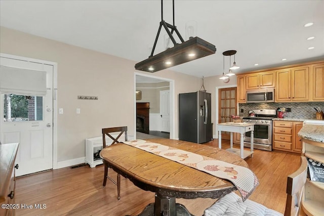 kitchen featuring recessed lighting, stainless steel appliances, a fireplace, light wood-style floors, and decorative backsplash