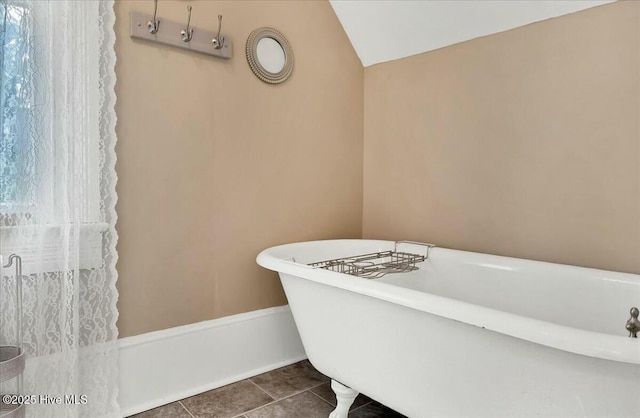 full bathroom with tile patterned flooring, a freestanding bath, lofted ceiling, and baseboards