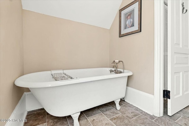 full bath featuring lofted ceiling, a freestanding tub, and baseboards