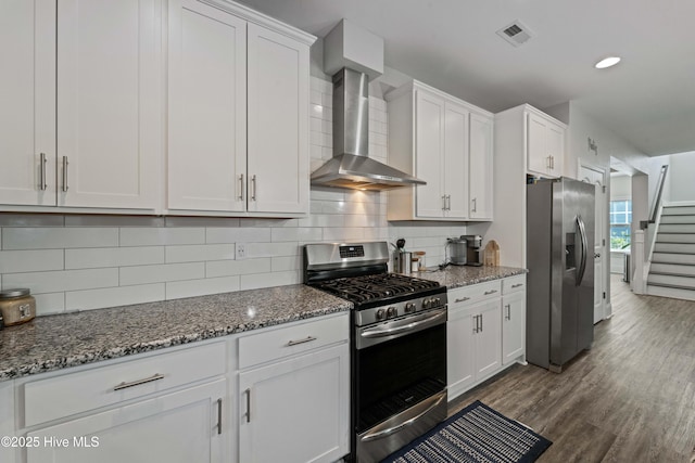 kitchen with white cabinetry, wall chimney range hood, dark stone counters, and appliances with stainless steel finishes