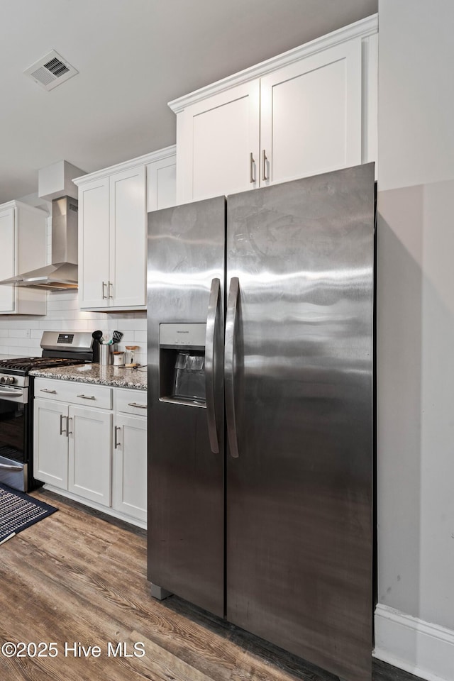 kitchen with wall chimney exhaust hood, appliances with stainless steel finishes, stone counters, decorative backsplash, and white cabinets