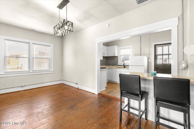 kitchen with decorative light fixtures, tasteful backsplash, white cabinetry, white refrigerator, and dark wood-type flooring