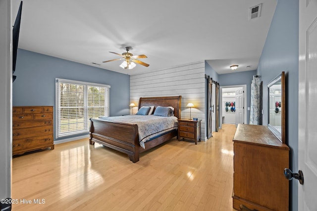 bedroom featuring light wood-style flooring, wooden walls, visible vents, and ceiling fan