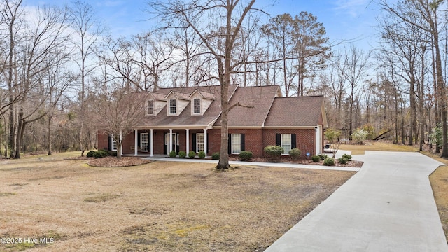 cape cod home with brick siding, covered porch, driveway, and a shingled roof