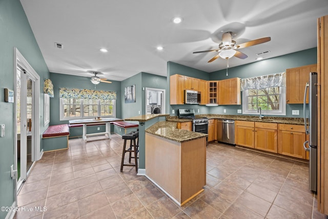 kitchen featuring ceiling fan, dark stone counters, a kitchen breakfast bar, a peninsula, and stainless steel appliances