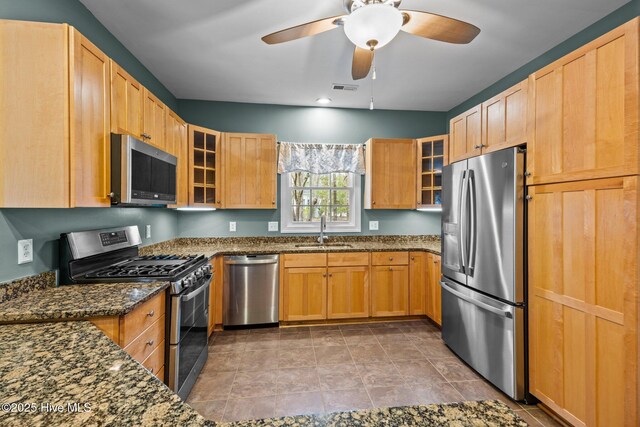 kitchen featuring visible vents, a sink, dark stone counters, appliances with stainless steel finishes, and glass insert cabinets