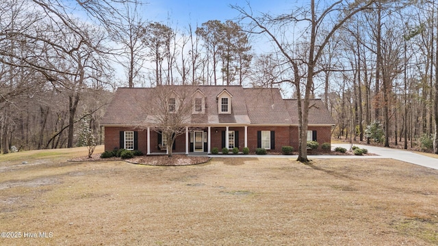 new england style home with brick siding, a porch, concrete driveway, and a front lawn