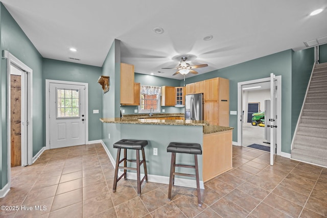 kitchen with glass insert cabinets, a peninsula, stainless steel fridge, stone countertops, and a sink