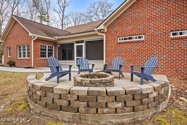 back of property featuring brick siding, a shingled roof, an outdoor fire pit, a sunroom, and a patio