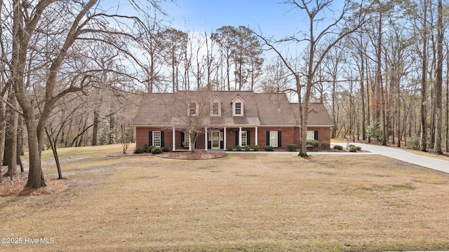 cape cod-style house with brick siding, covered porch, driveway, and a front lawn