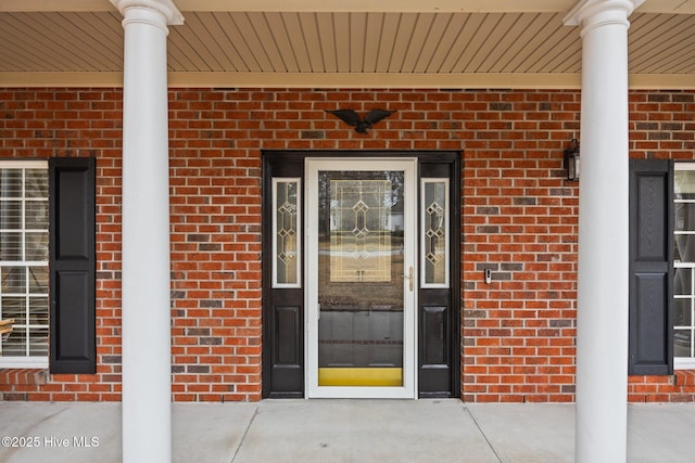 view of exterior entry featuring brick siding and covered porch