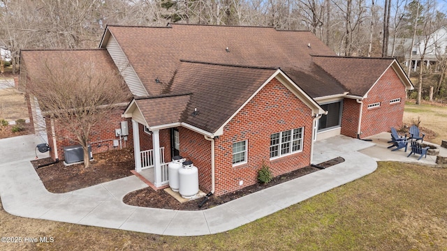 view of side of property featuring brick siding, a patio area, a shingled roof, and a yard