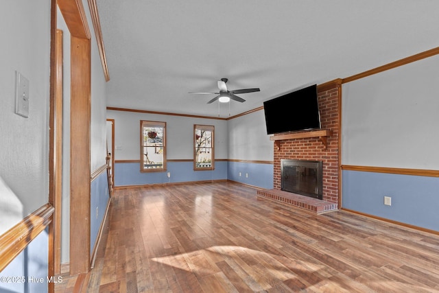 unfurnished living room featuring hardwood / wood-style flooring, a fireplace, ornamental molding, and a ceiling fan