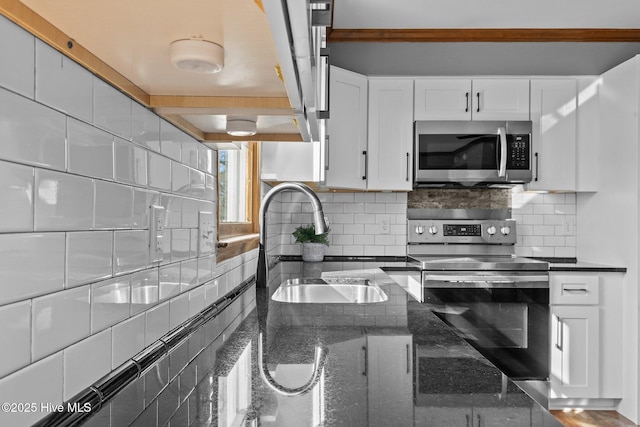 kitchen with tasteful backsplash, white cabinets, dark stone counters, appliances with stainless steel finishes, and a sink