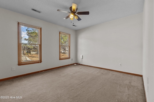 carpeted spare room featuring ceiling fan, visible vents, baseboards, and a textured ceiling