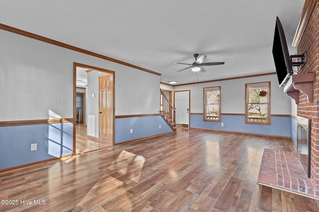 living area featuring a fireplace, ceiling fan, a textured ceiling, wood finished floors, and stairs