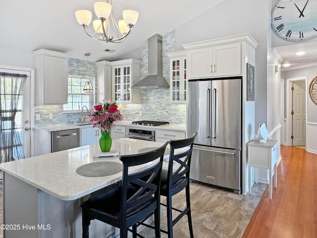 kitchen featuring wall chimney exhaust hood, a center island, appliances with stainless steel finishes, pendant lighting, and white cabinets